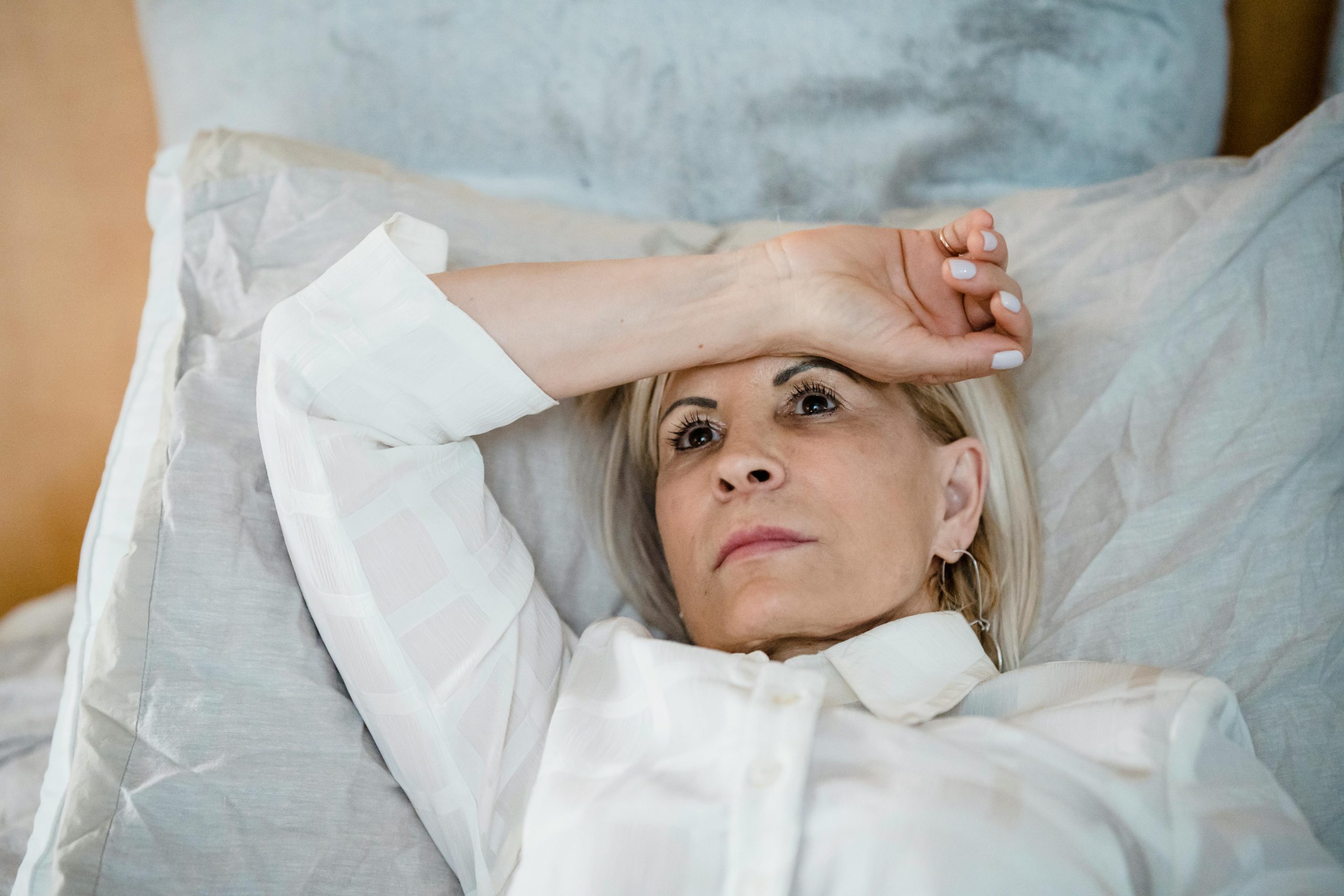 Woman in her late 40s lying in bed, hand on forehead, struggling with sleep disruption — a familiar feeling for women navigating menopause